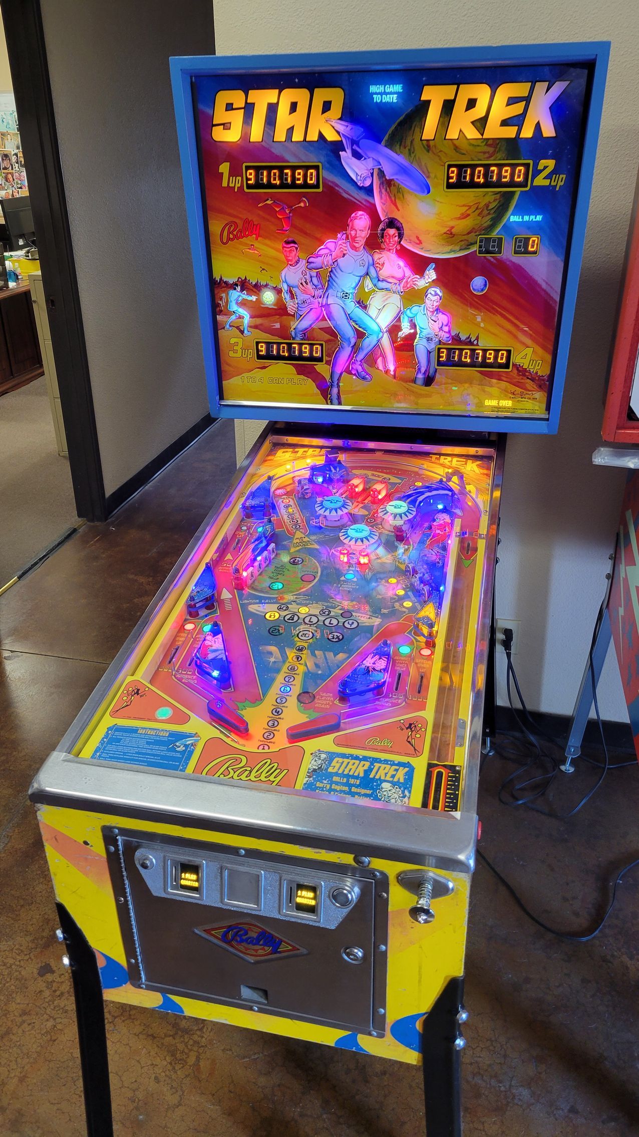 A star trek pinball machine is sitting on a wooden floor in a room.