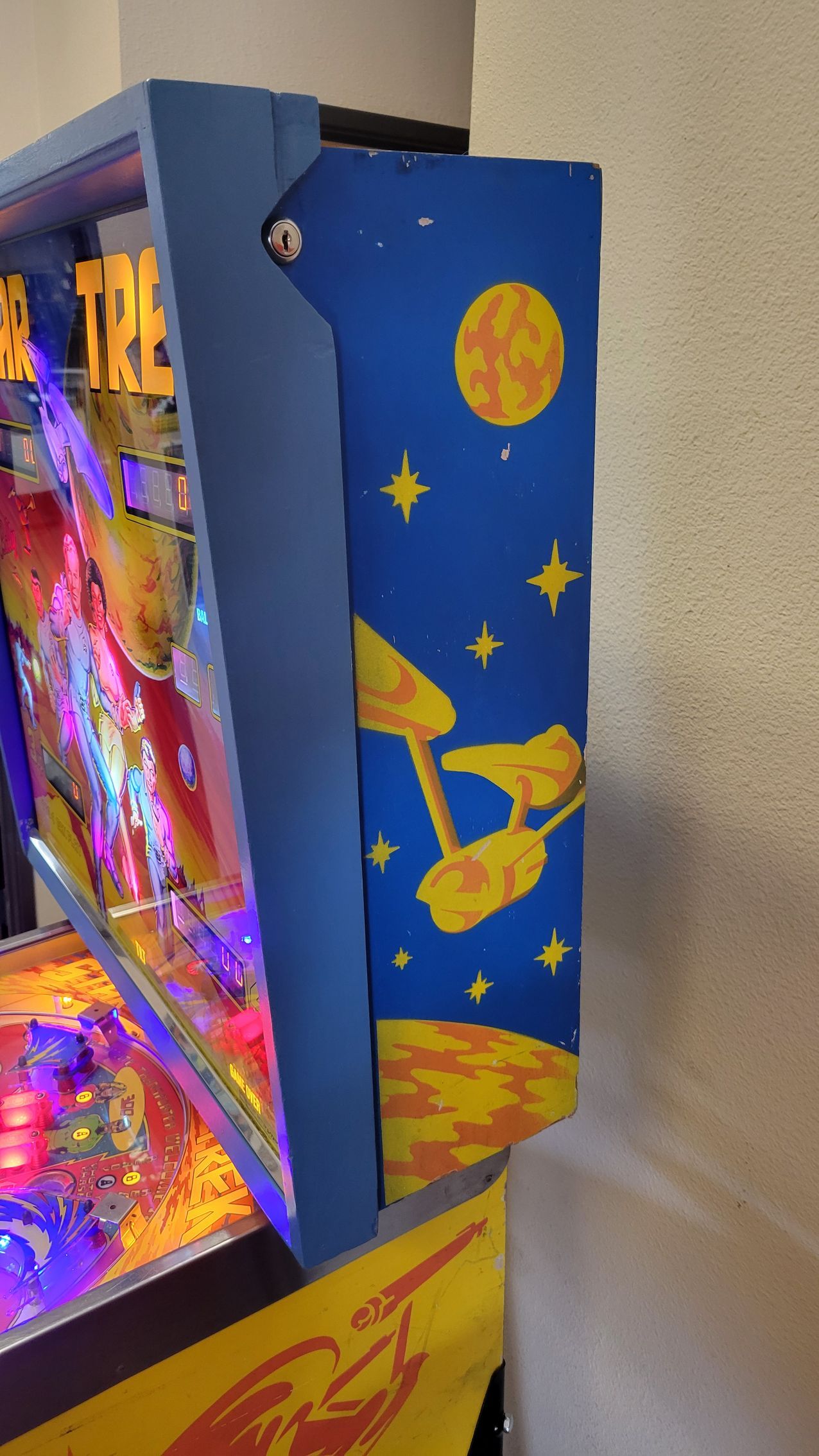 A pinball machine is sitting on a table next to a wall.