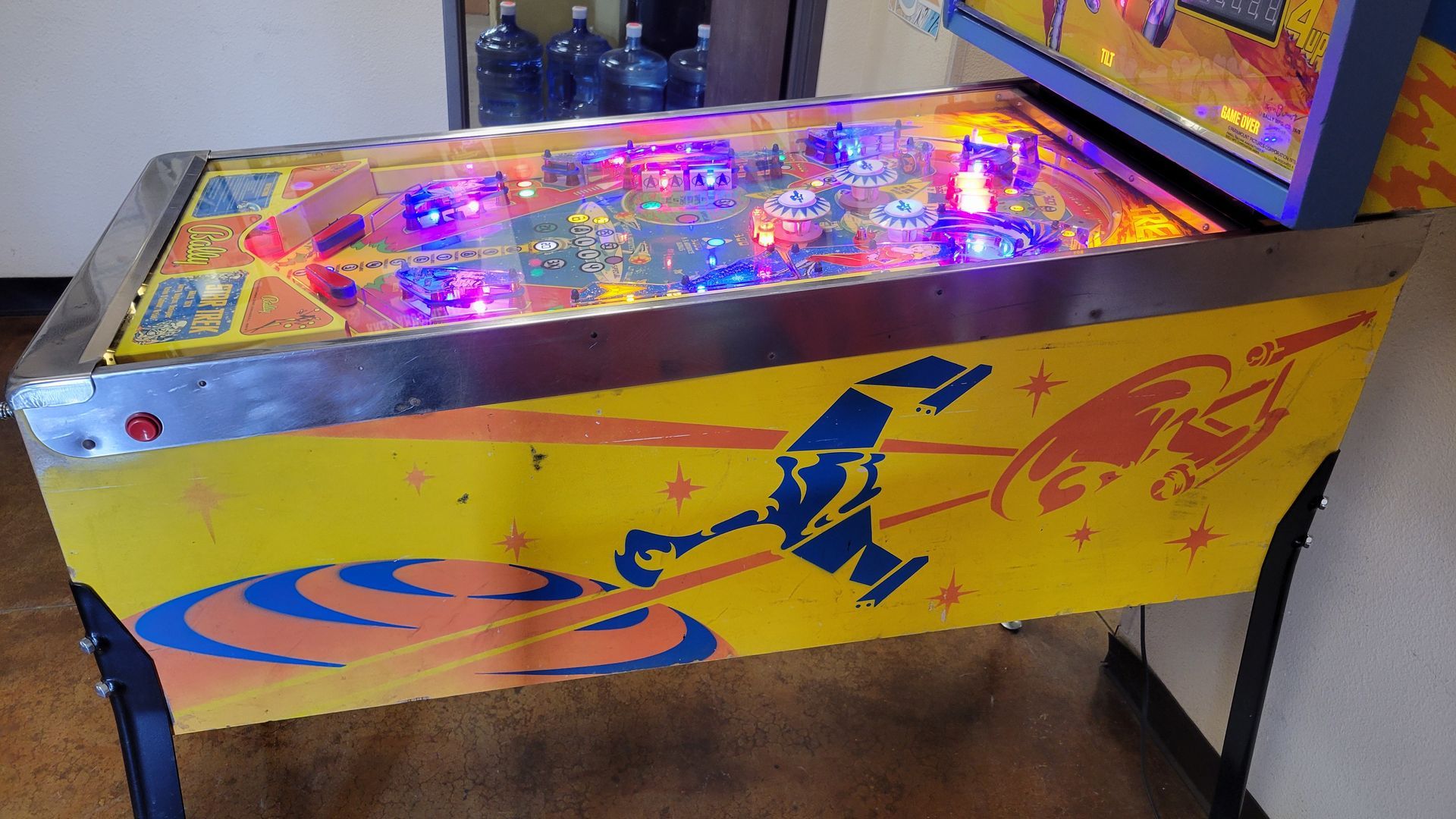 A yellow pinball machine with a rocket on it