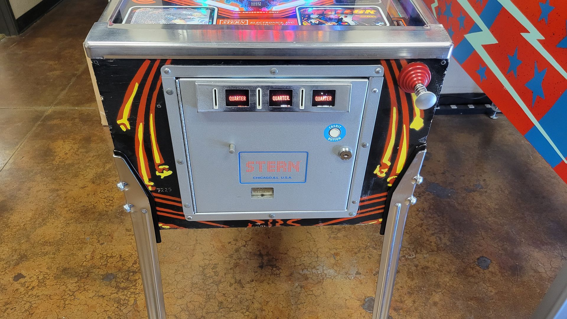 A pinball machine is sitting on a concrete floor.