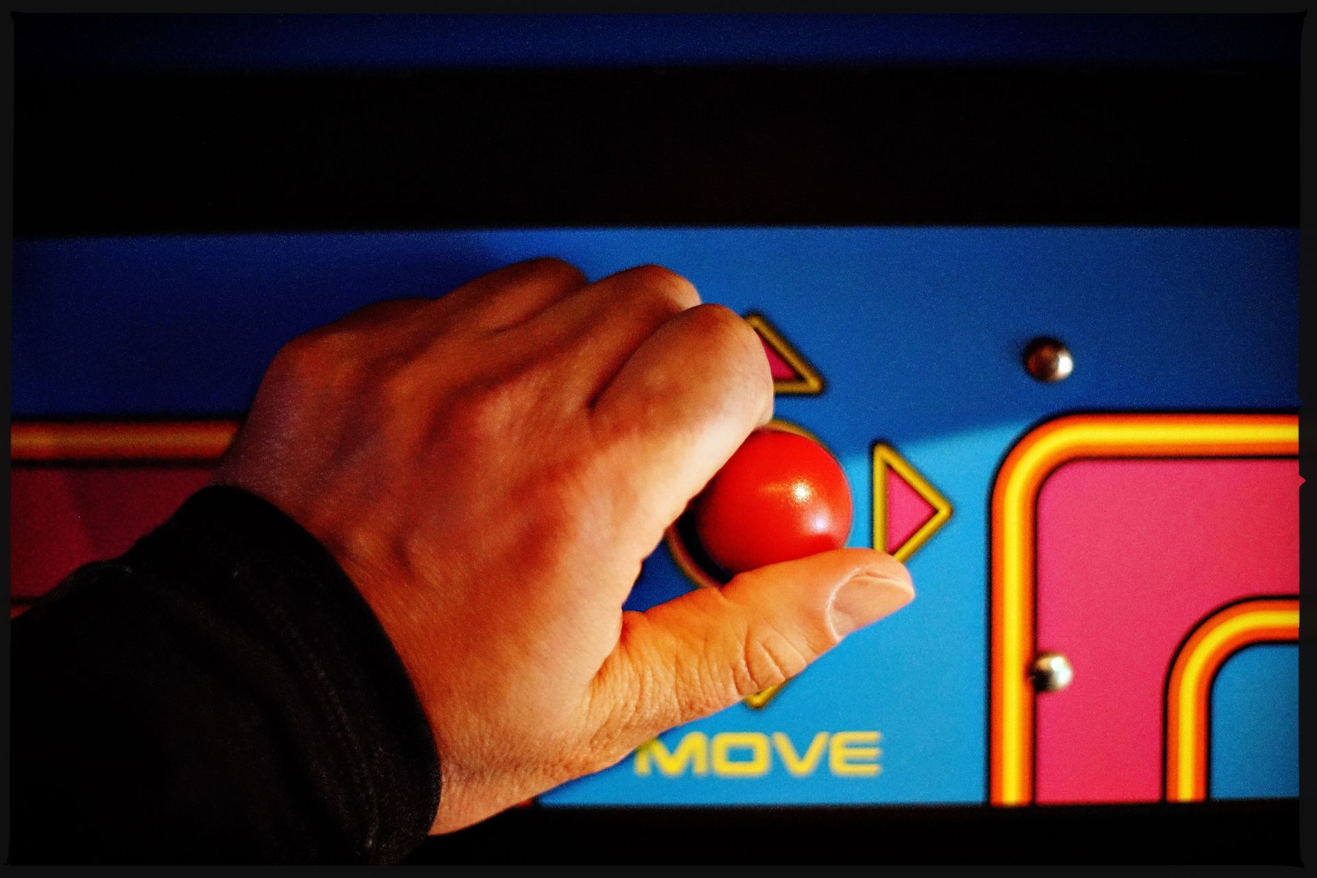 Hand gripping red joystick on arcade game machine.