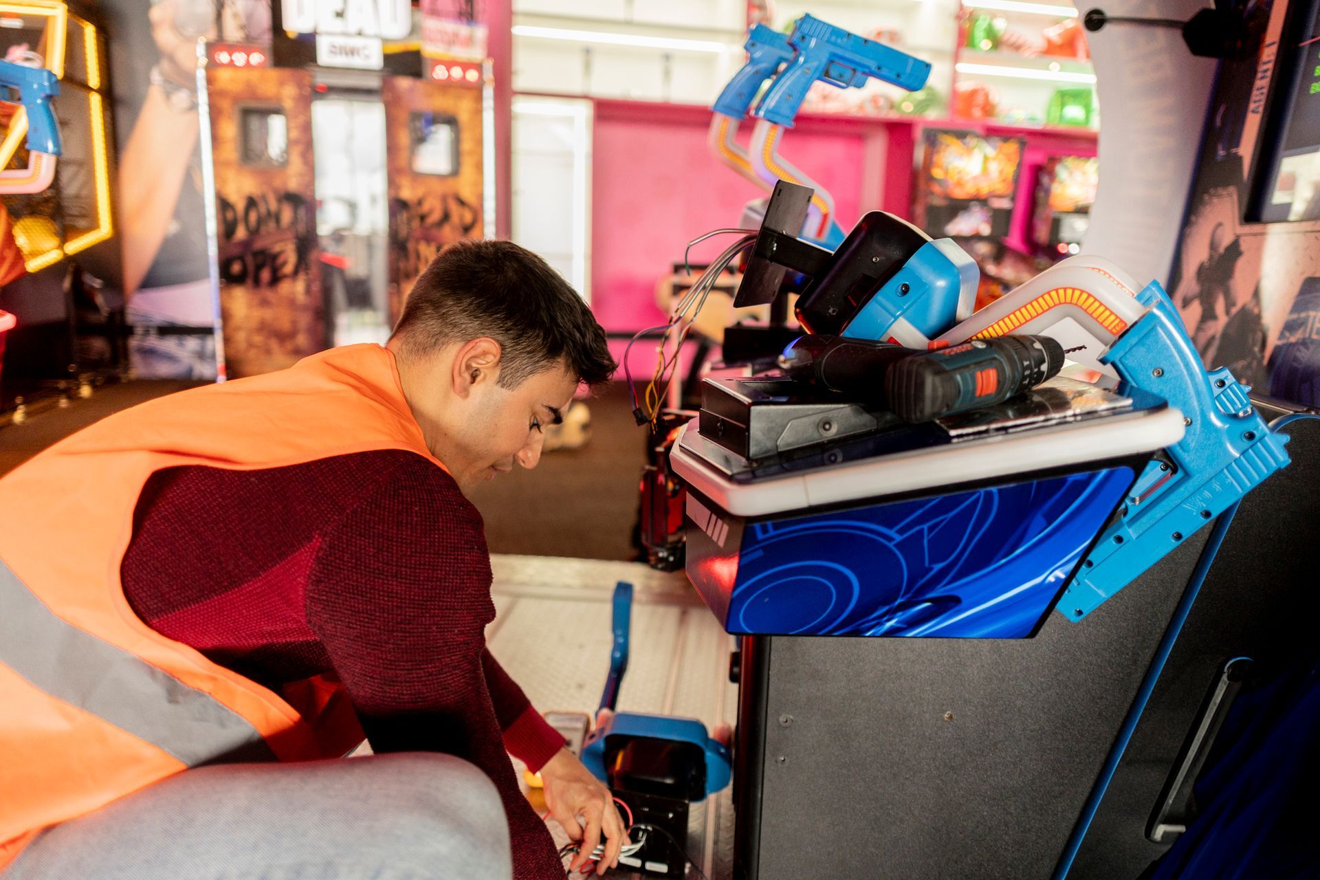 Technician performing commercial arcade repairs on gaming console with blue gun controllers.
