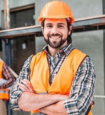 Construction worker with crossed arms, wearing an orange hard hat and safety vest, smiling.
