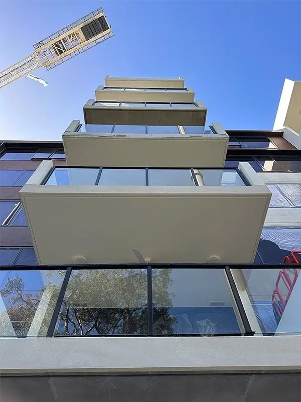 Modern building with several rectangular balconies extending outward, glass railings, blue sky.