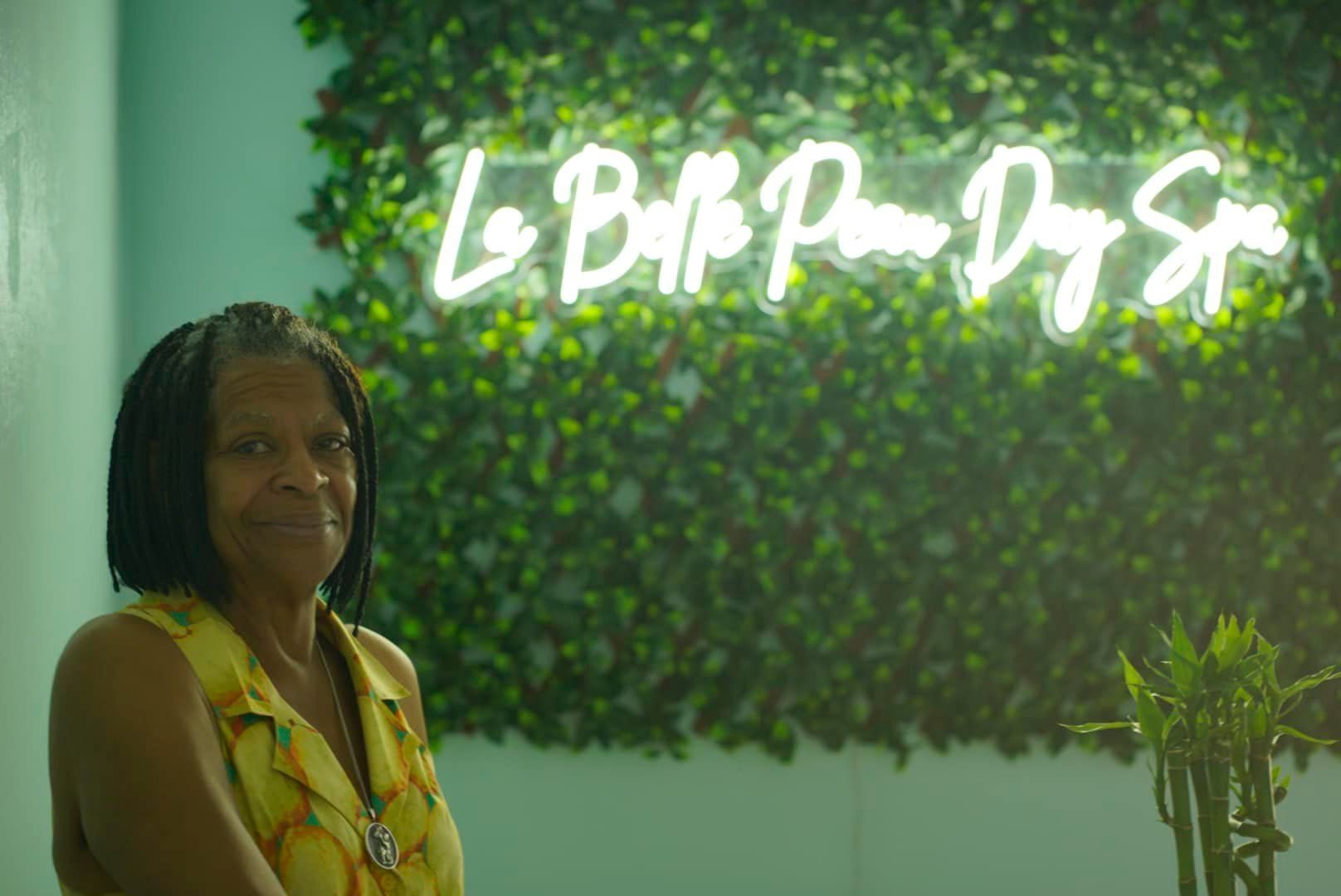A woman is sitting in front of a neon sign.