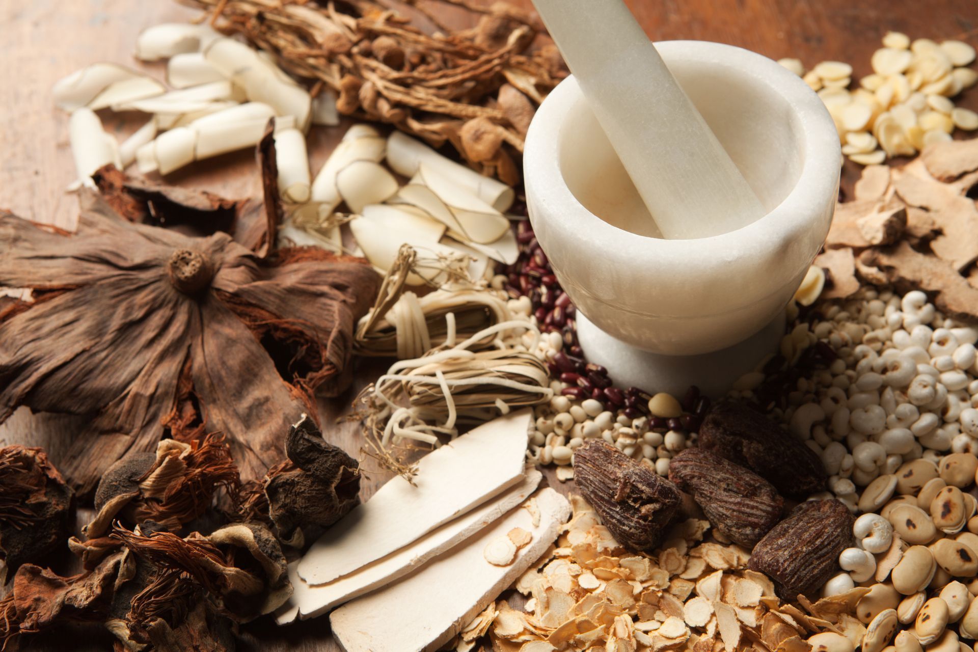 A mortar and pestle surrounded by various herbs and spices on a wooden table.