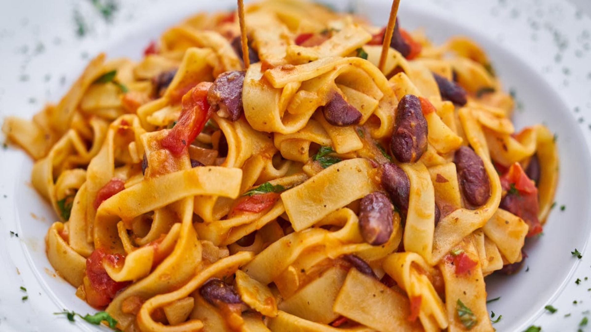 Plato de pasta con fideos anchos, salsa roja y frijoles en un plato blanco.