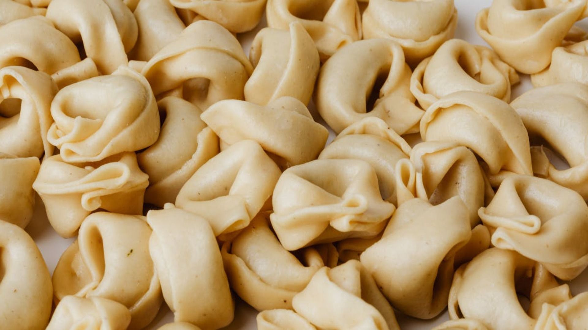 Primer plano de pasta tortellini cruda, de color beige marfil, que llena el marco.