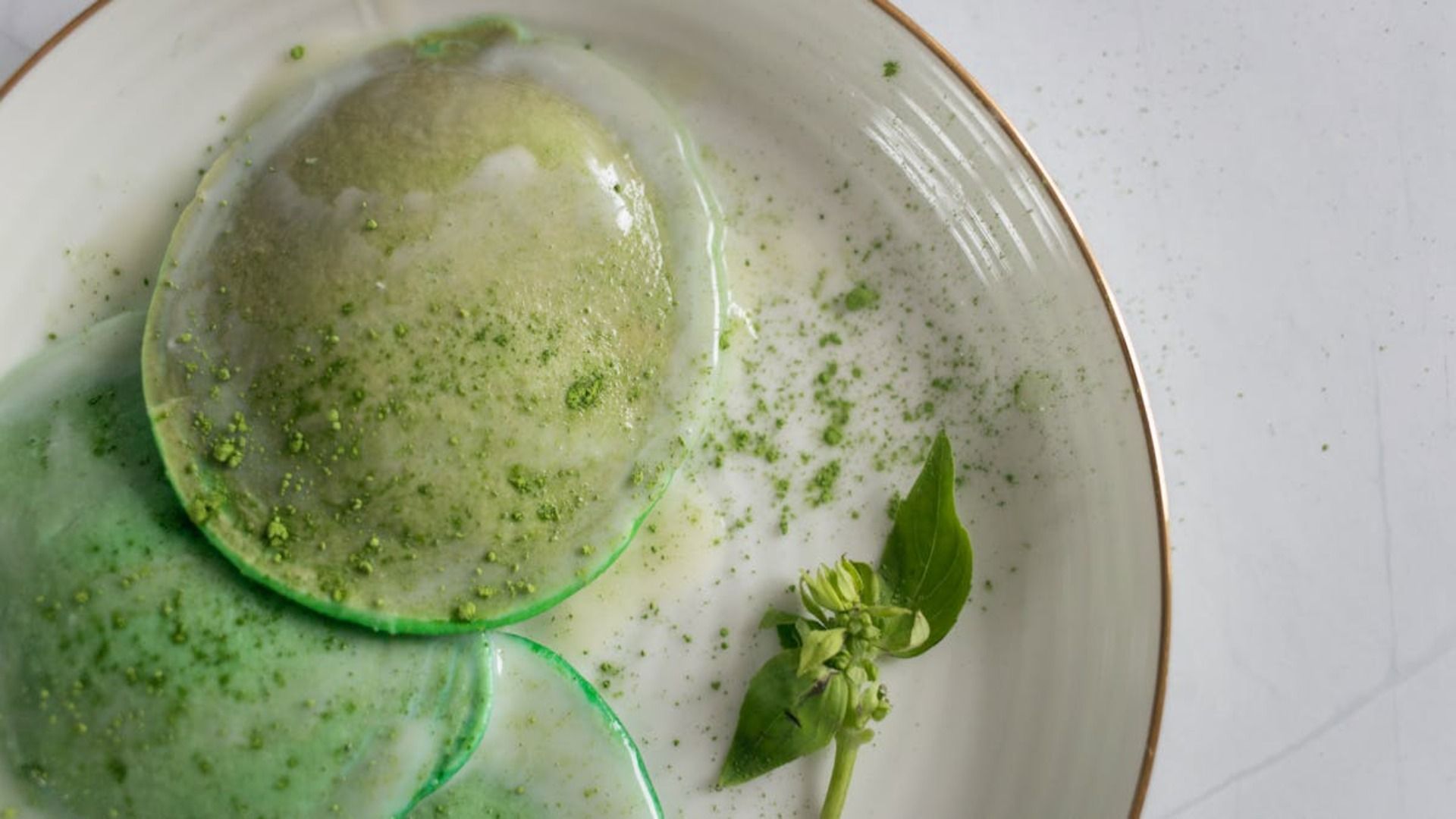 Ravioles verdes en un plato blanco, espolvoreados con polvo verde y una ramita de hojas verdes.