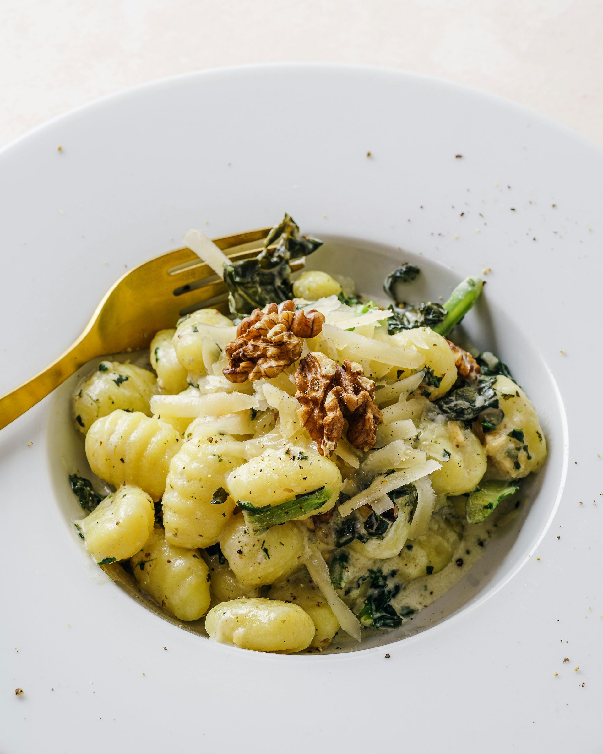 Ñoquis con verduras, nueces y queso en un bol blanco con un tenedor dorado.
