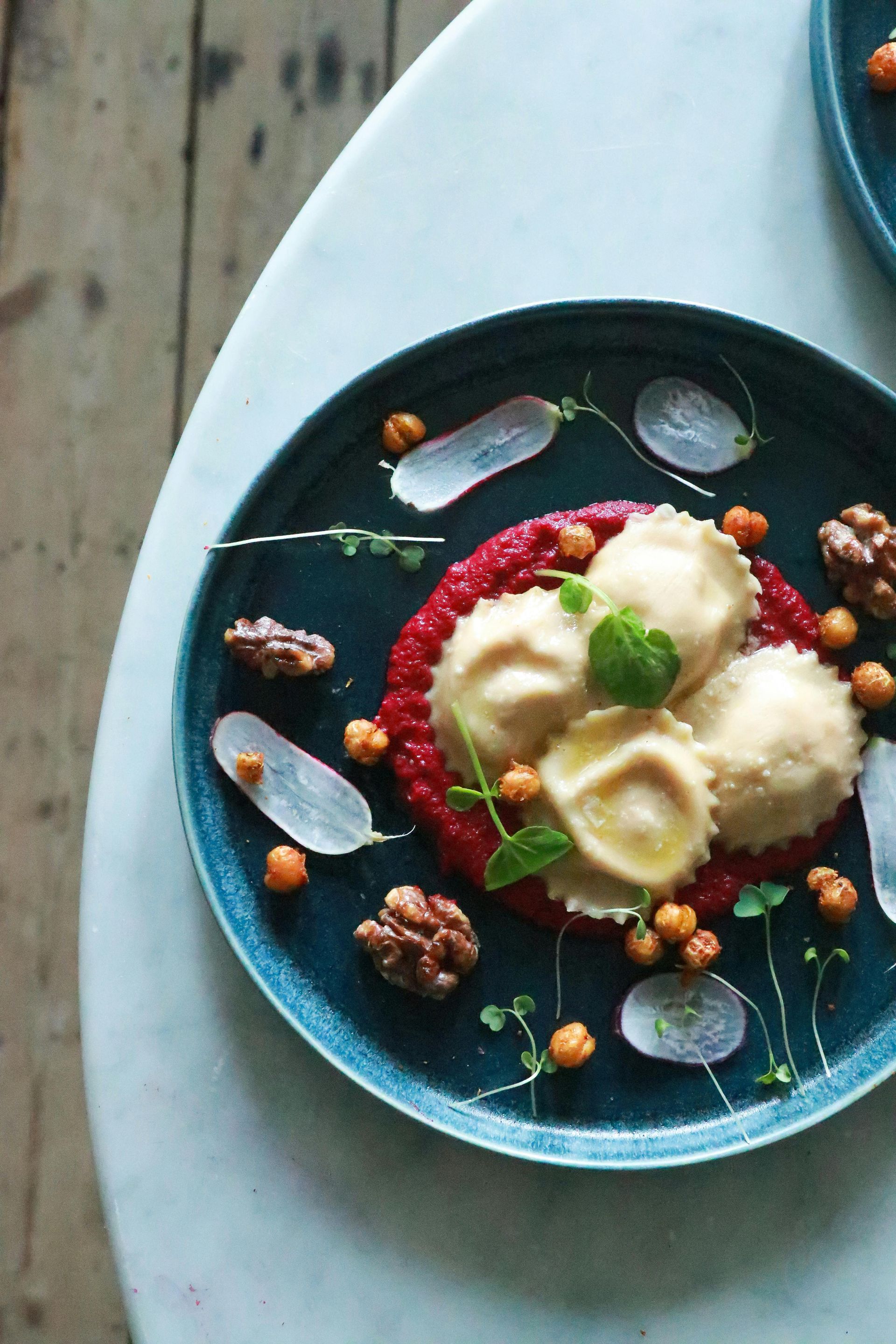 Raviolis con salsa de remolacha, nueces y garbanzos en un plato azul; servido en una mesa ligera.