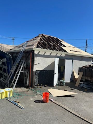 A building with a partially removed roof under construction on a sunny day; a ladder and materials are nearby.