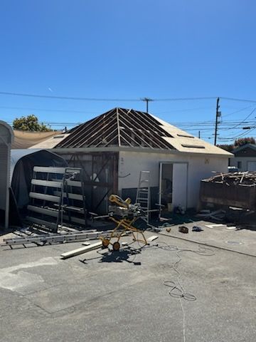 A building under construction with a partially completed roof, tools scattered around on a sunny day.