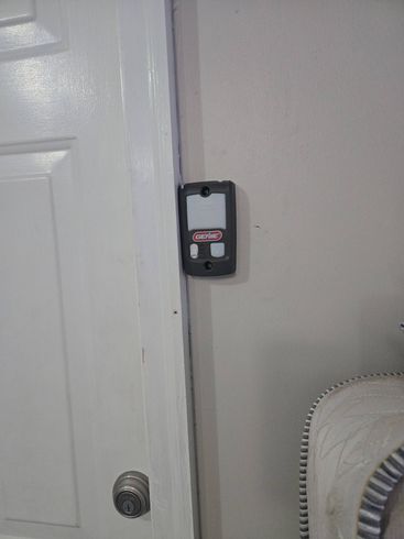 Black wall-mounted device beside a white door on a beige wall.