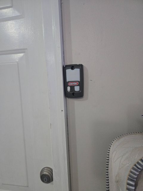 Black wall-mounted device beside a white door on a beige wall.