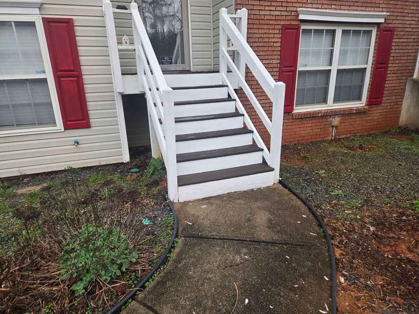 White front steps with railings leading to a house entrance, beside red shutters and a curved walkway.