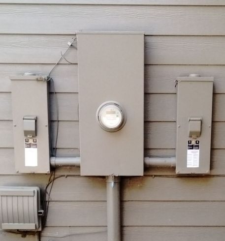 Three gray utility meters mounted on beige siding with a central round meter.