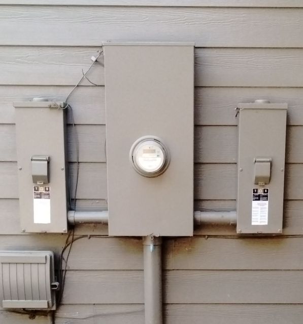 Three gray utility meters mounted on beige siding with a central round meter.