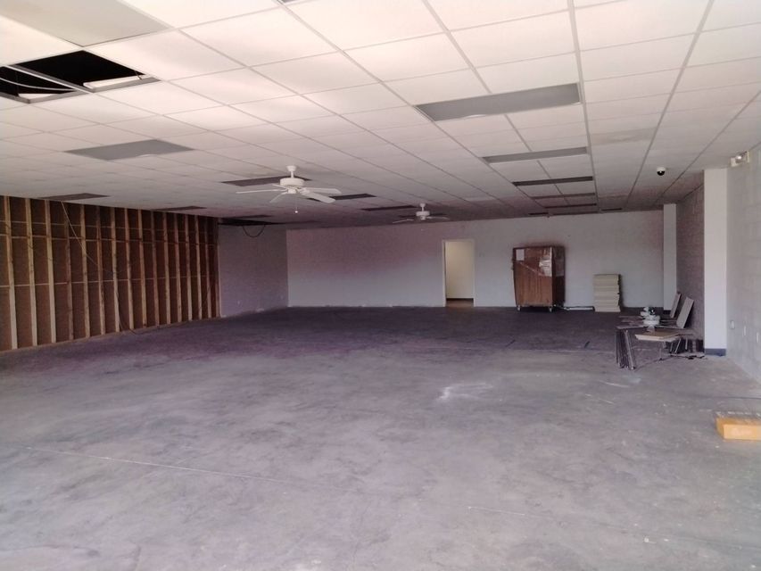 Empty unfinished office with bare ceiling tiles, gray floor, and a few chairs against the wall.