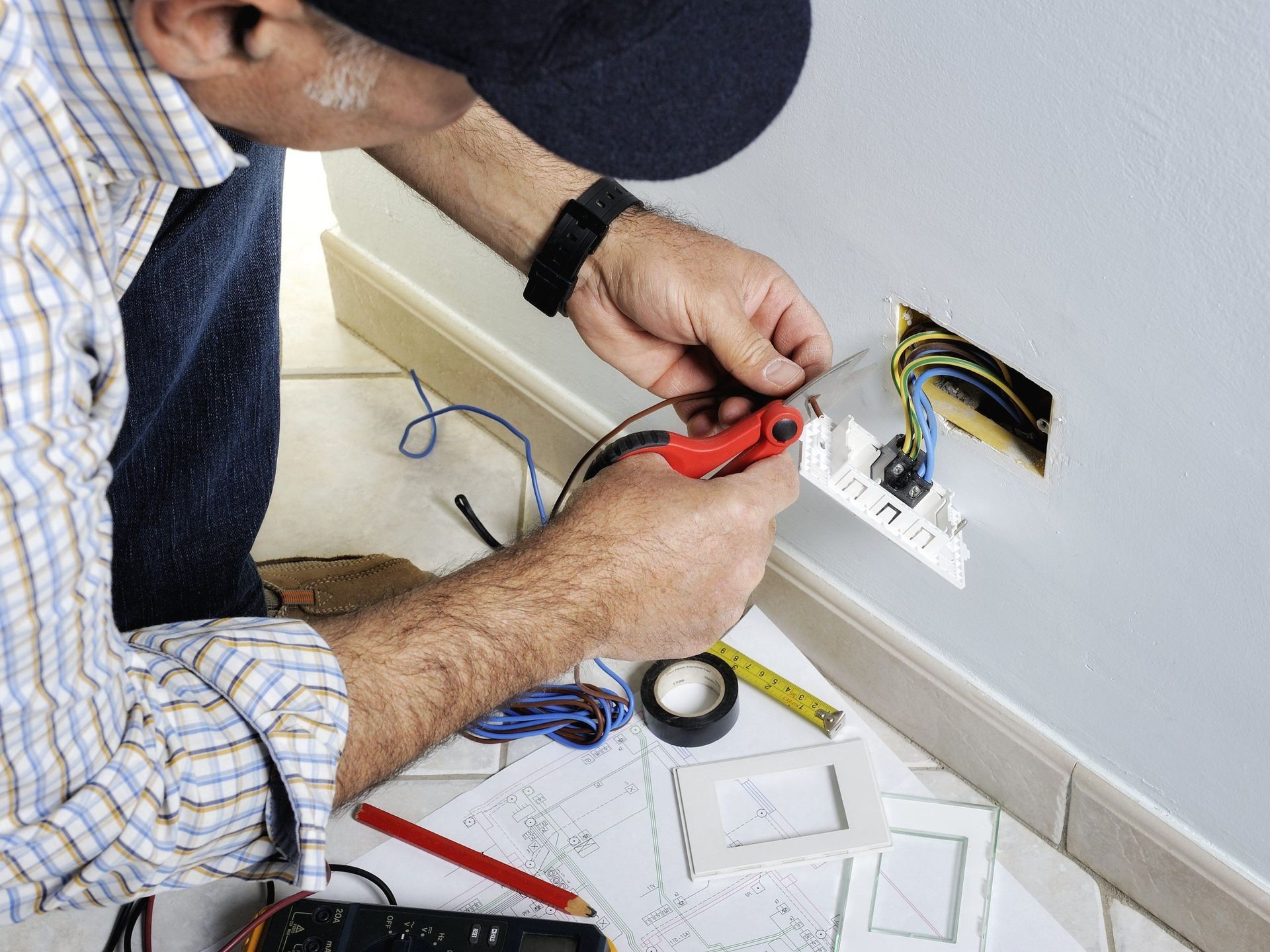 Electrician connecting wires in a wall outlet box with a red-handled tool.
