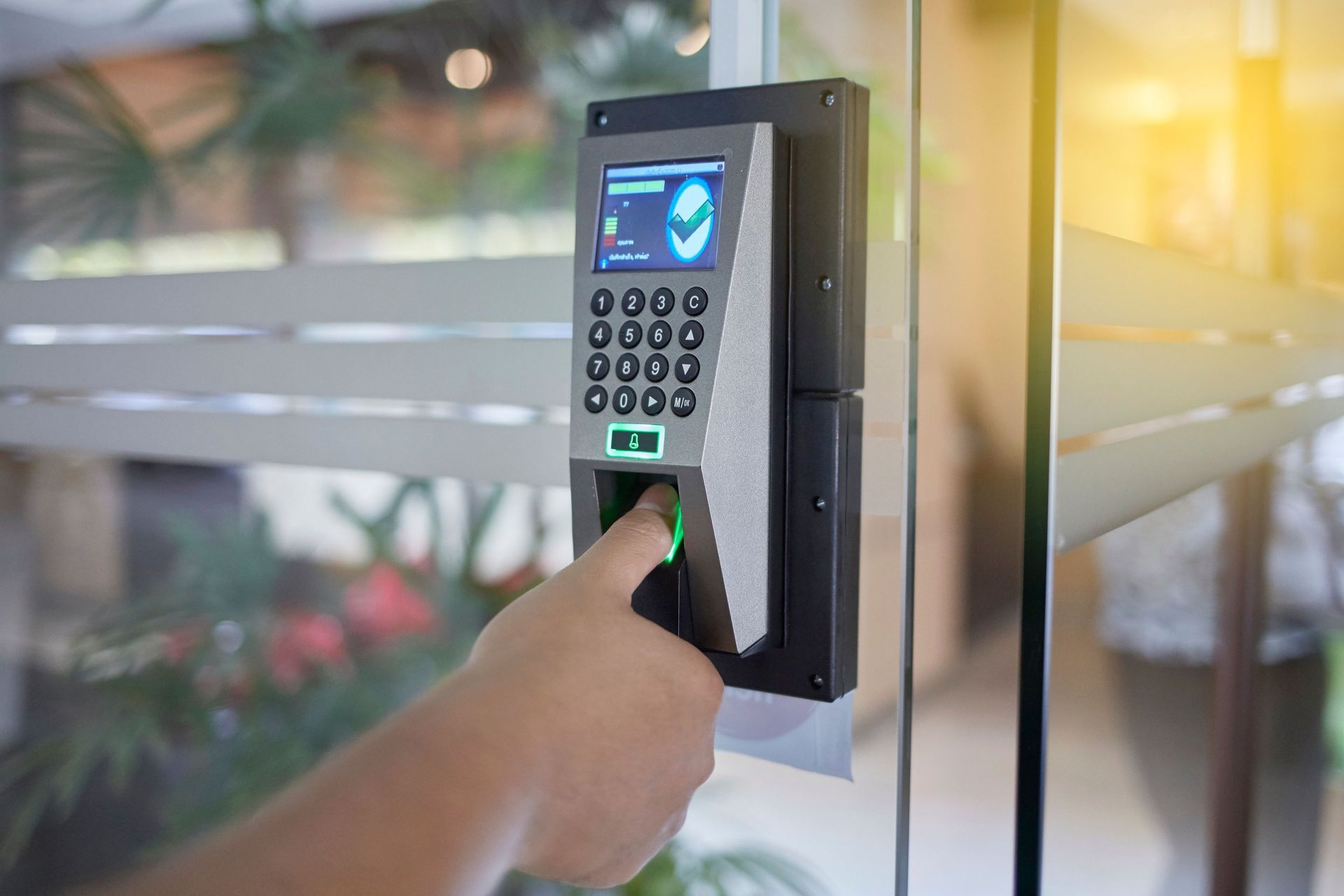 Hand using a fingerprint scanner on a door access keypad beside a glass entrance
