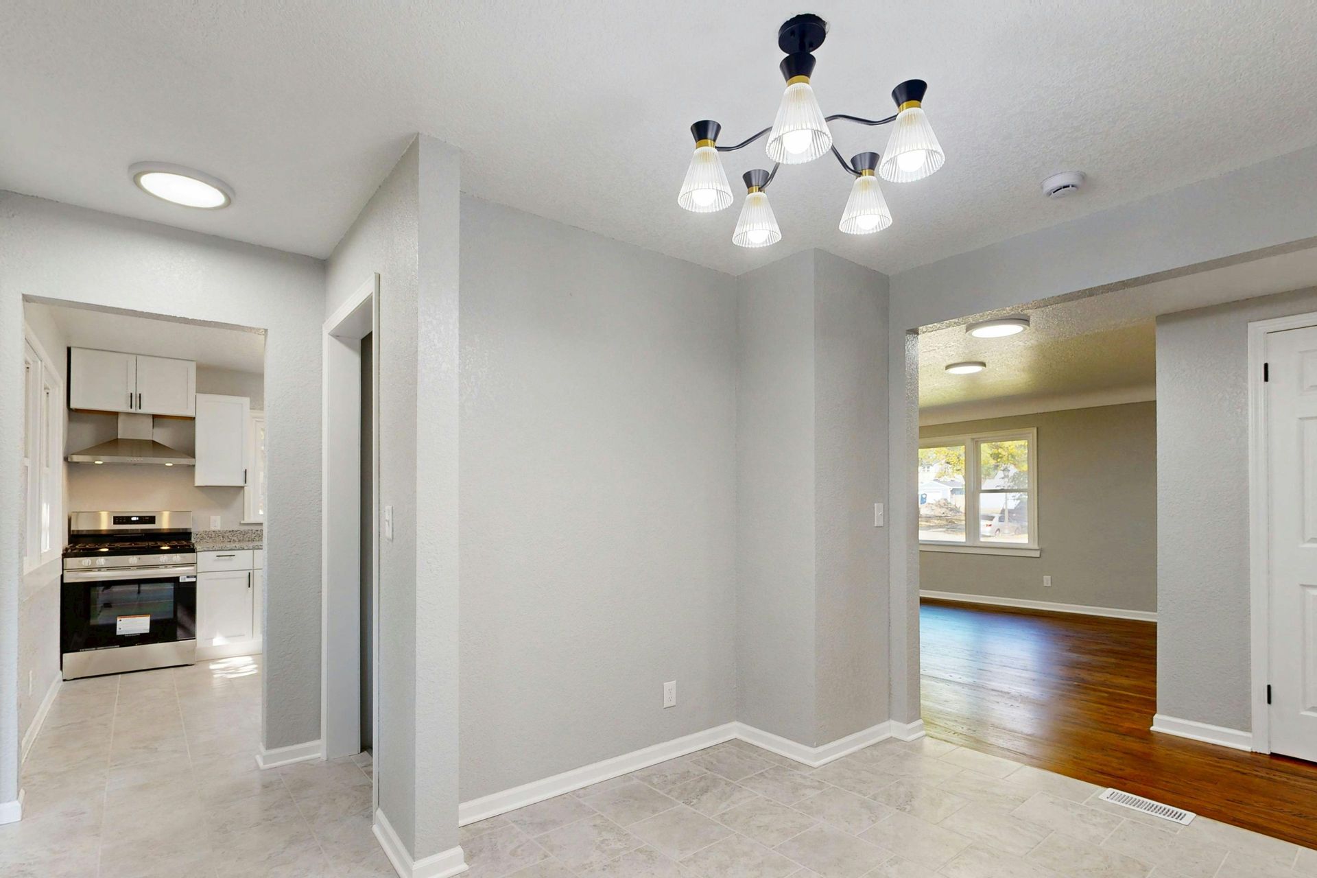 Empty white dining area with carpet, chandelier, and view into a kitchen and hardwood-floored room