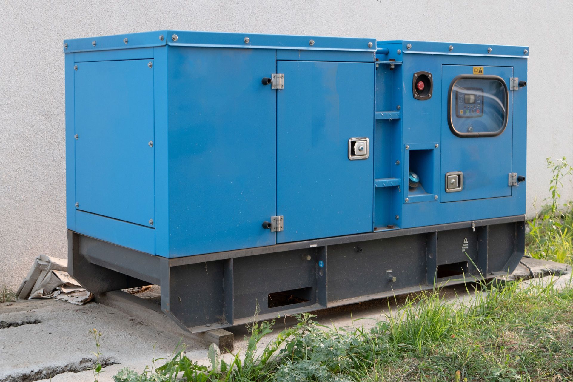 Blue industrial generator unit on a concrete pad beside a building, with grass in the foreground Blue industrial generator unit on a concrete pad beside a building, with grass in the foreground