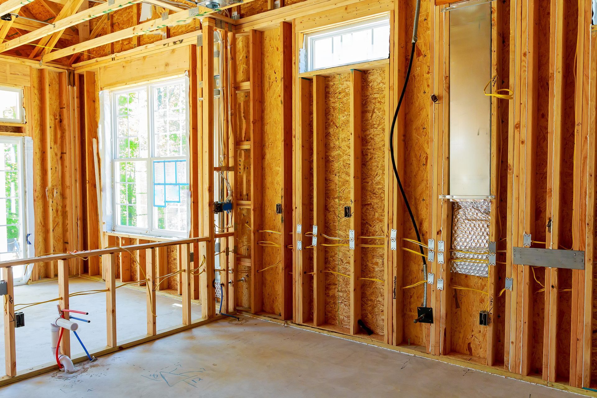 Unfinished room with exposed wooden framing, insulation, windows, and a concrete floor under construction.