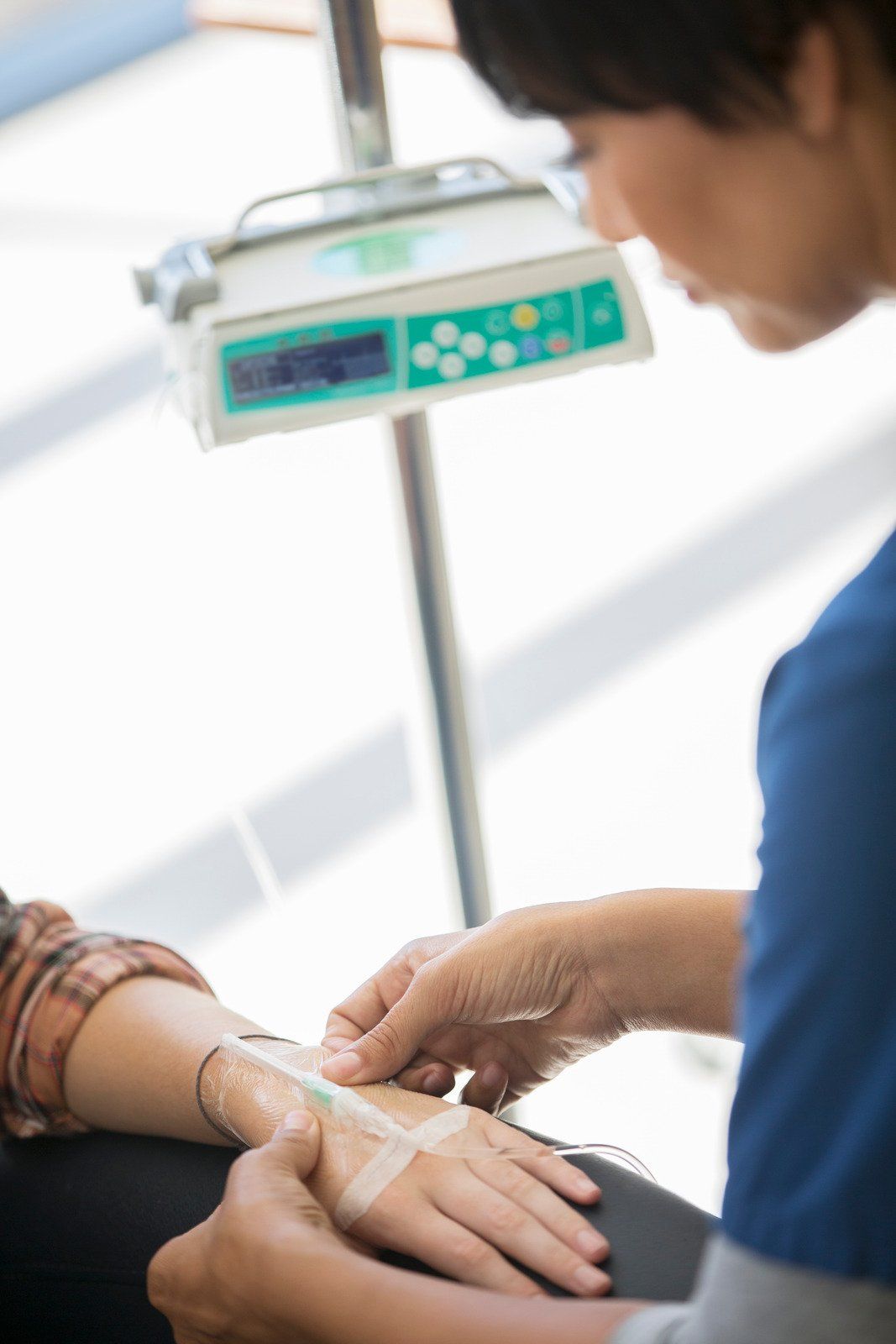 Nurse securing IV line on patient's arm; IV pump in the background.