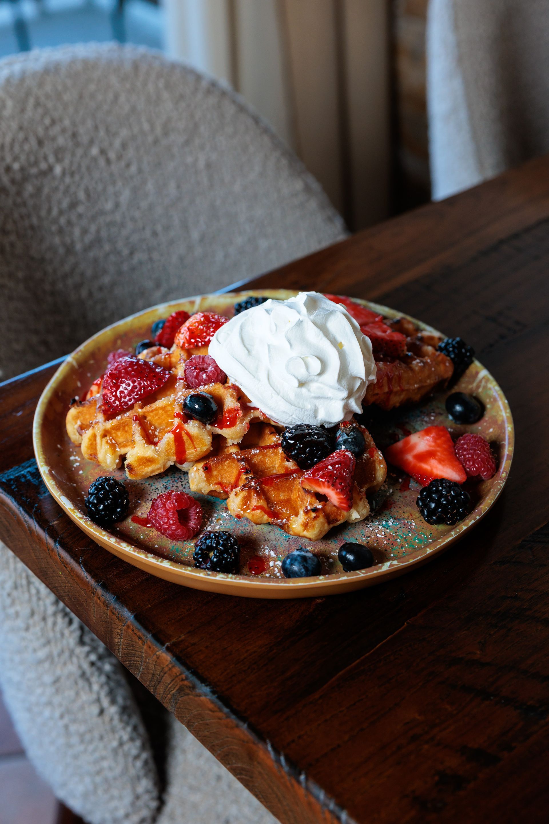 Waffles with berries and whipped cream on a plate on a wooden table.