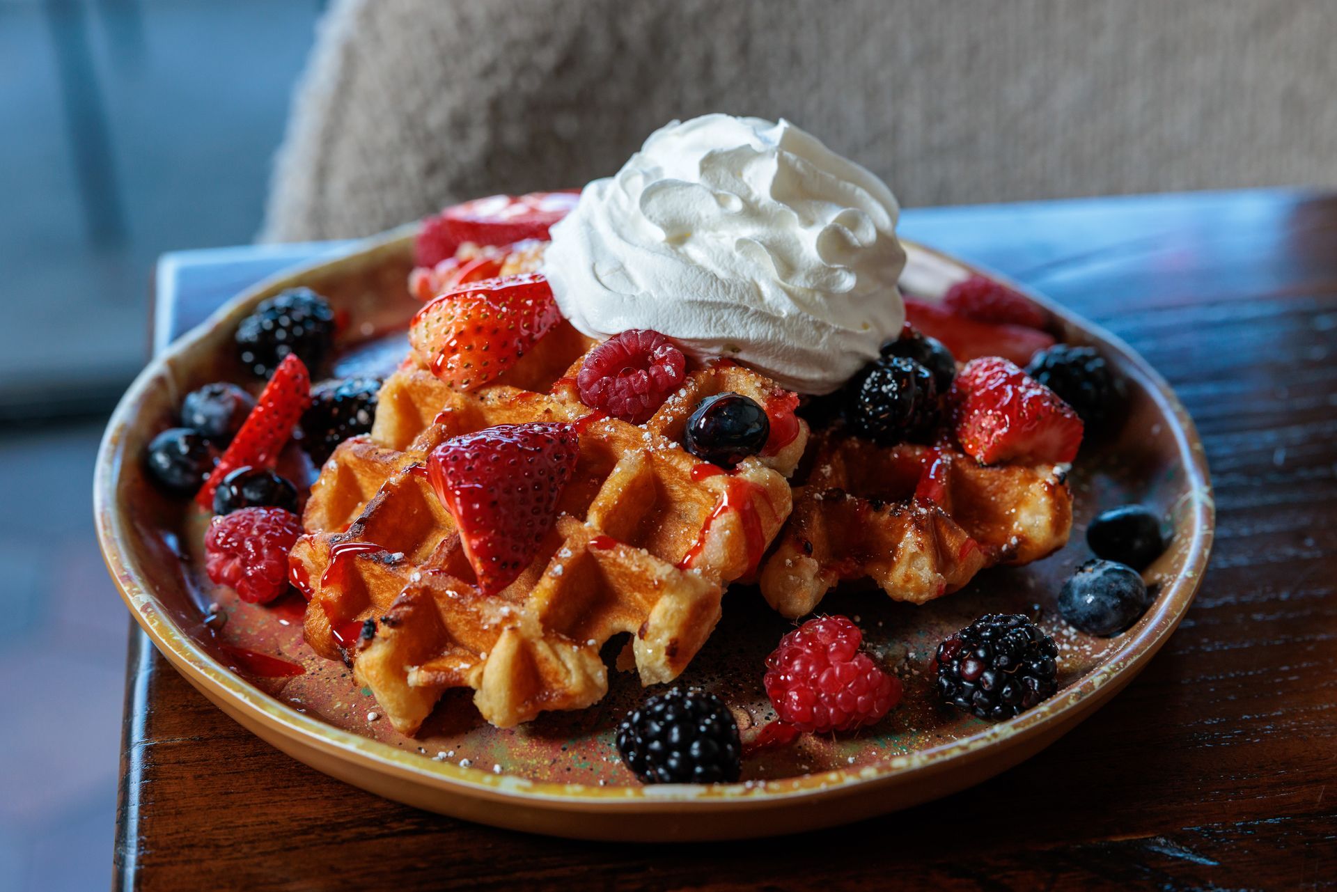 Waffles topped with strawberries, raspberries, blueberries, blackberries, and whipped cream on a plate.