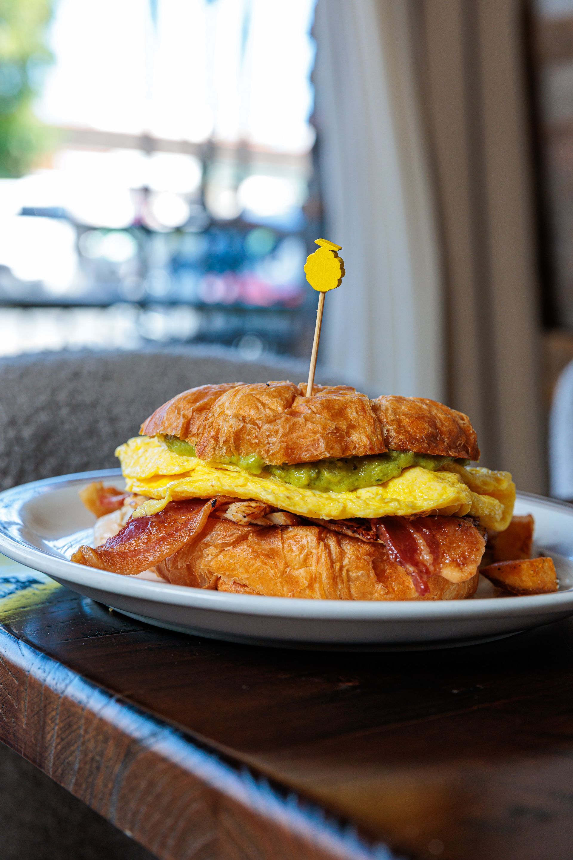 Croissant breakfast sandwich with bacon, egg, and avocado, on a white plate.