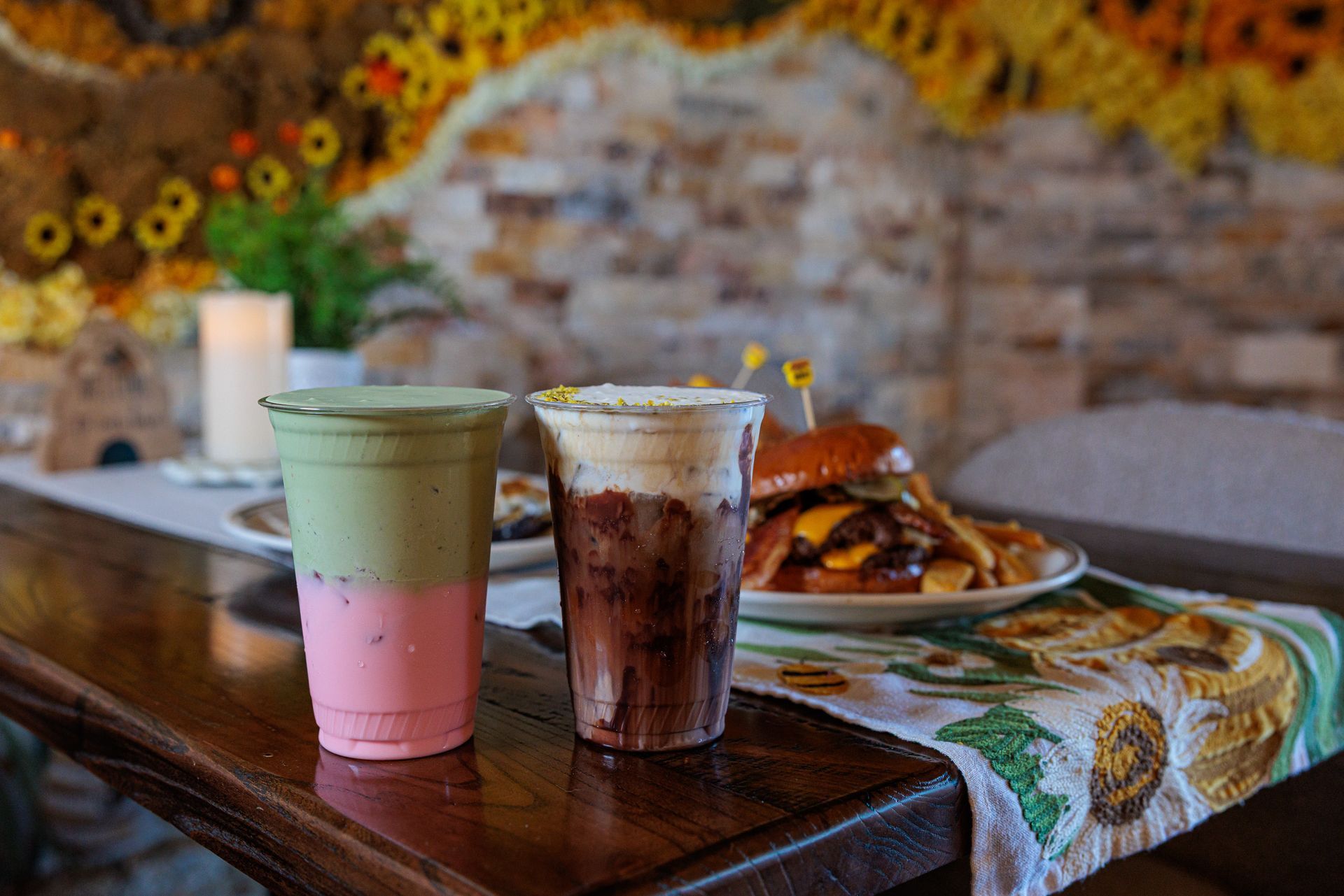Two layered drinks and a burger on a table with a floral tablecloth.