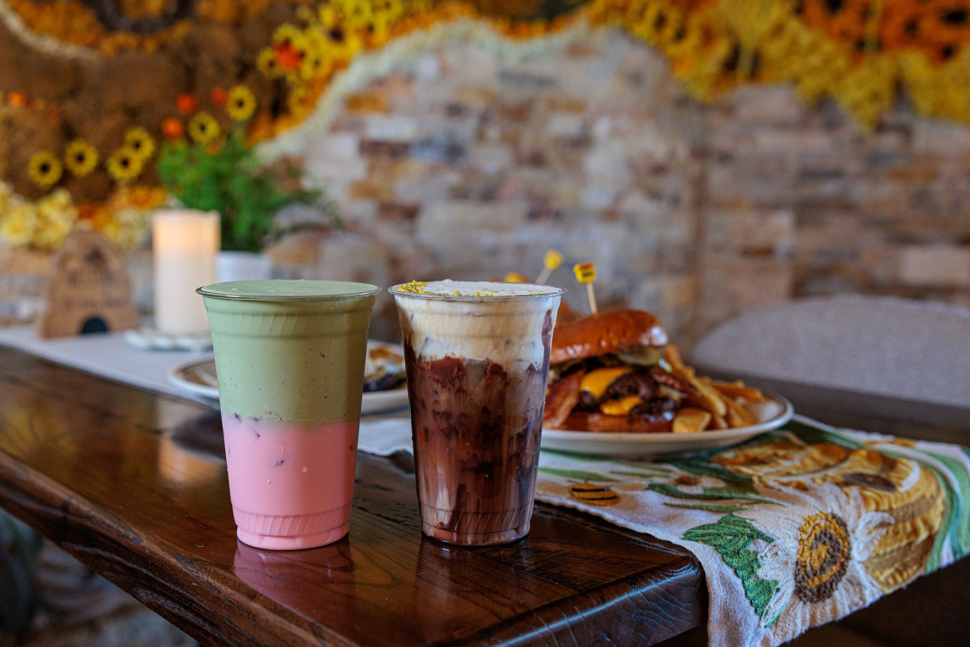 Two layered drinks and a burger on a table with a decorative backdrop.