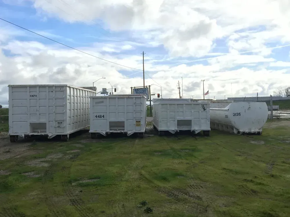 White dumpster containers on a grass field under a cloudy sky