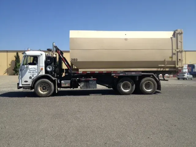 White truck with a beige container in a parking lot