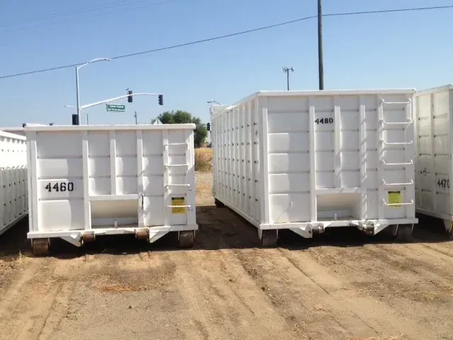 Two white dumpsters are sitting on dirt