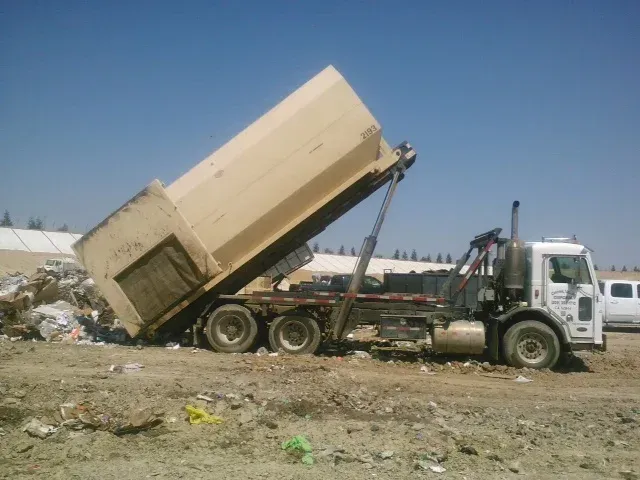 Dump truck with raised bed, dumping trash at a landfill on a sunny day