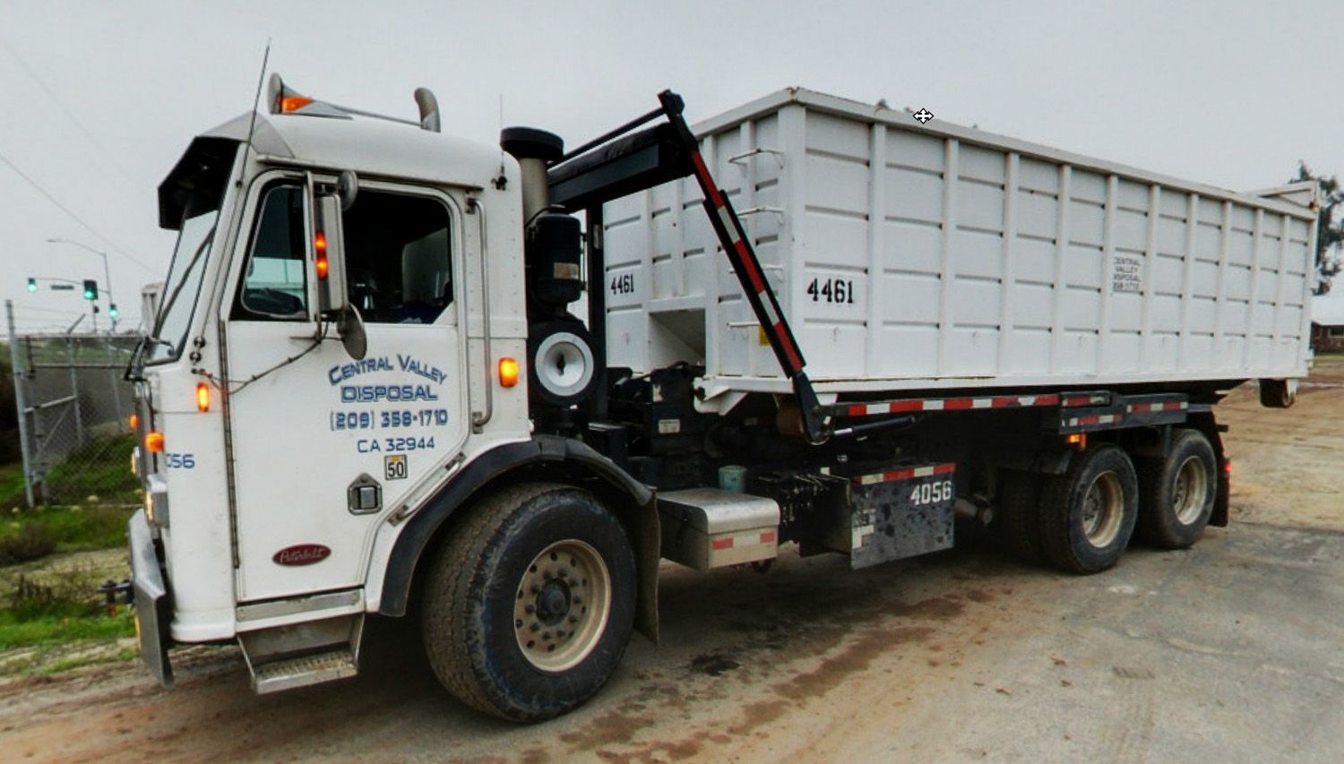 White garbage truck with a large container on a dirt road