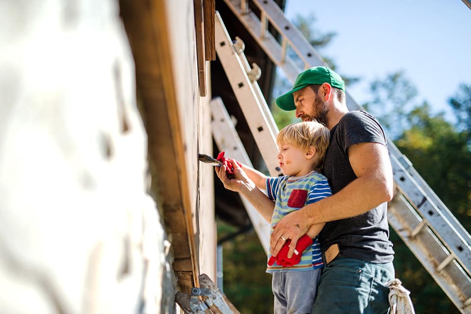 A man and his son paint an exterior wall as they complete an outdoor project.