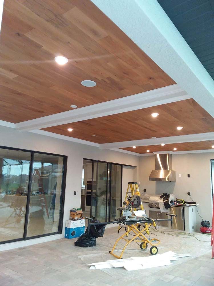 Wood-paneled ceiling with recessed lighting in a modern kitchen and patio area, still under construction.