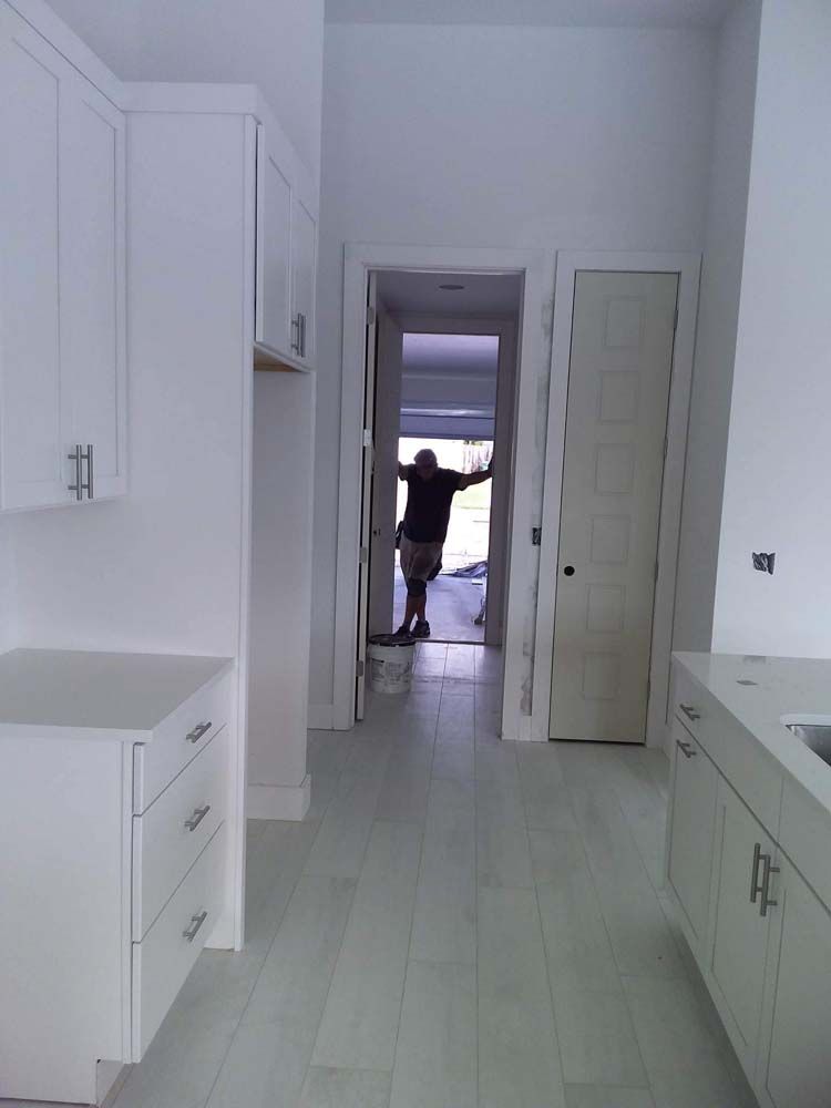 White kitchen with cabinets, a man in the doorway, and light-colored flooring.