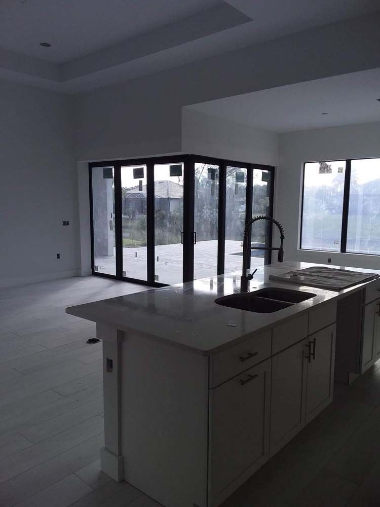 Kitchen island with sink, white cabinets, folding glass doors to backyard.
