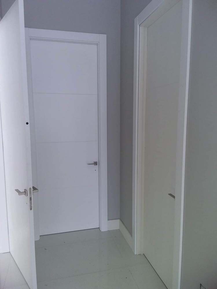 Three white doors in a hallway, with gray walls and floor. One door is open.