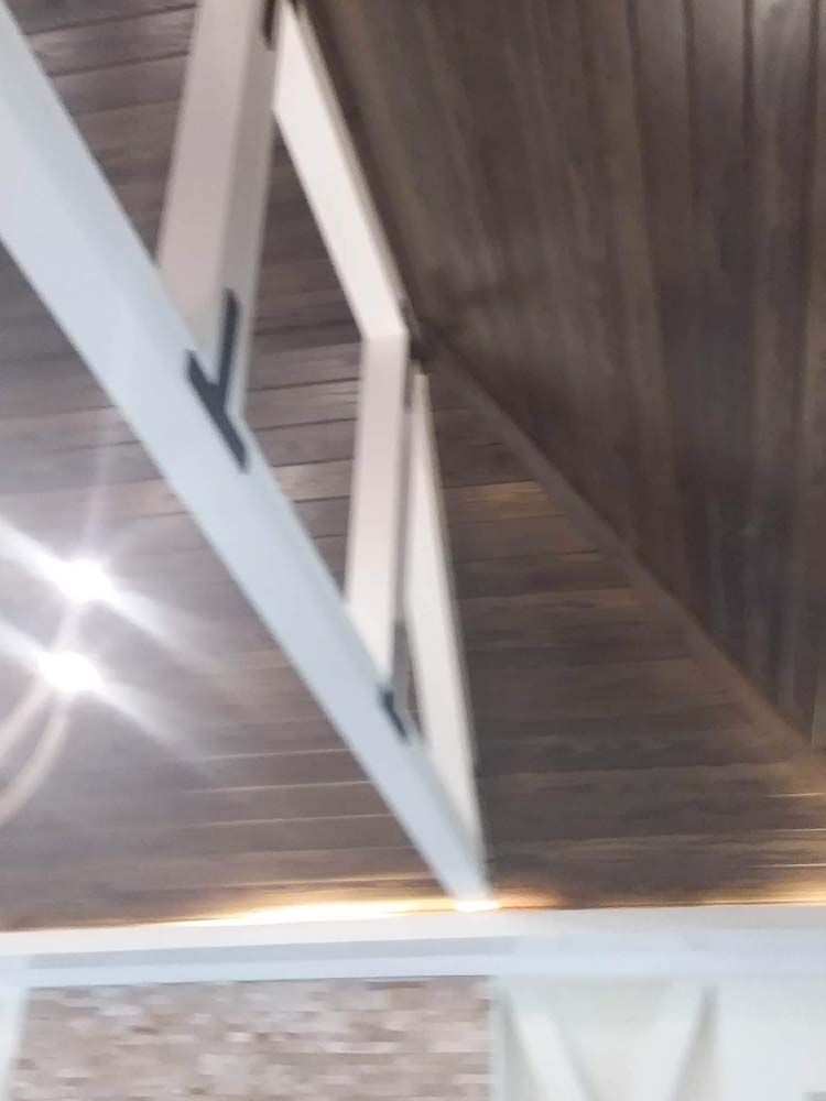 White rafters with black metal braces, supporting a dark wood ceiling.