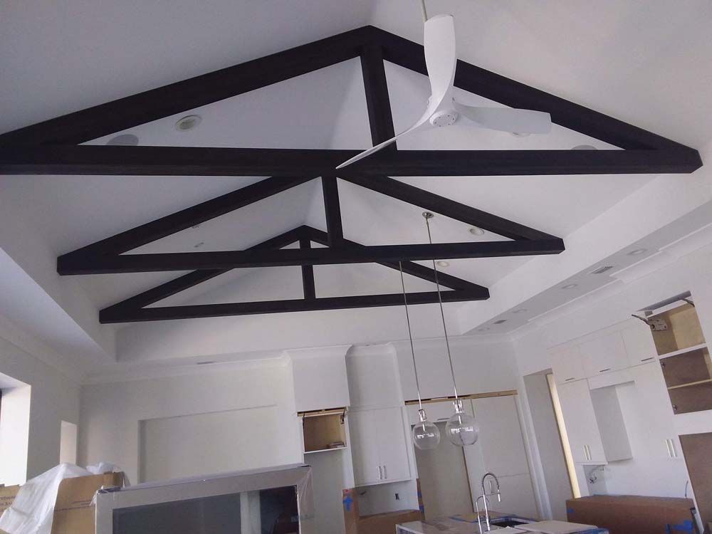 Dark wooden beams forming a triangular truss pattern on a white ceiling. Kitchen remodel in progress.