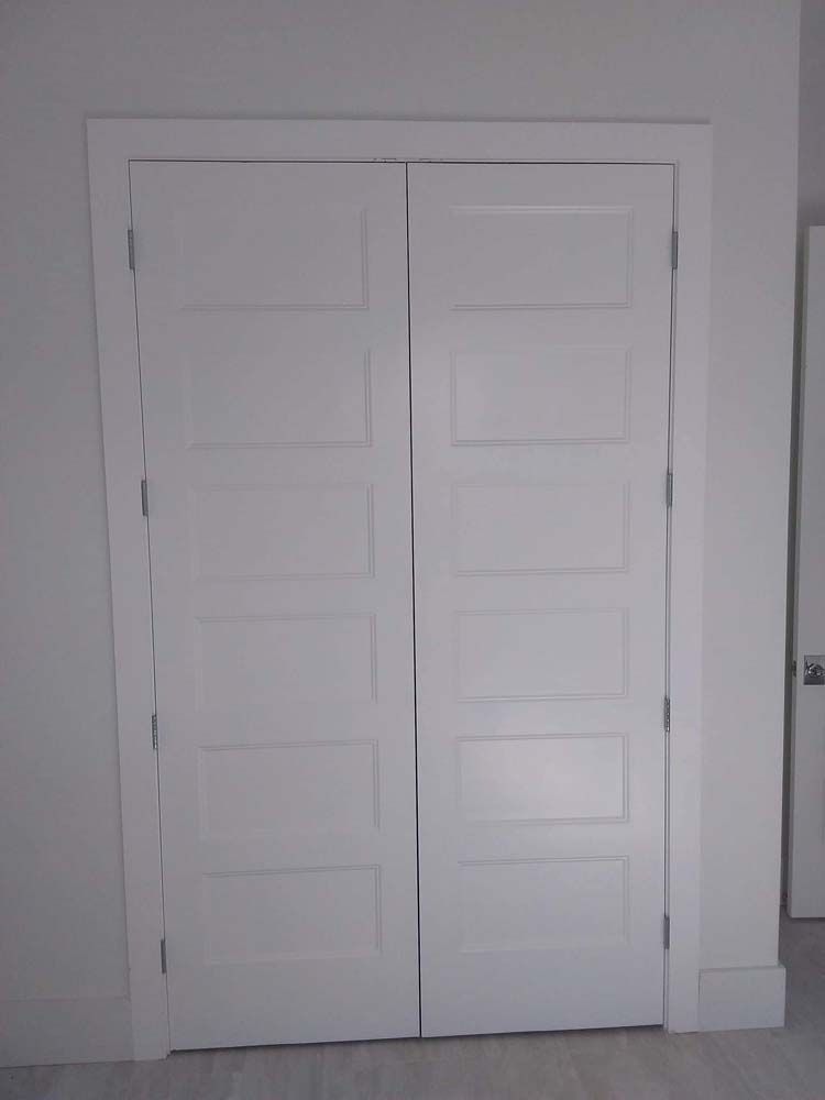 White bi-fold closet doors with five rectangular panels, surrounded by a white frame, in a room with light flooring.