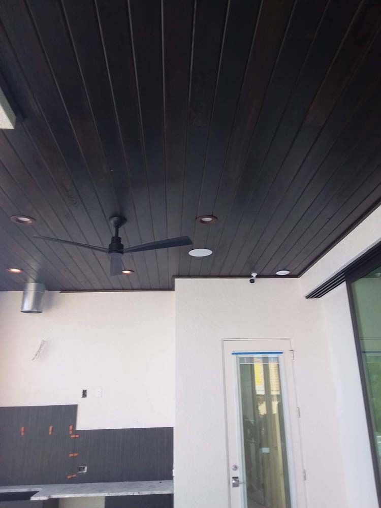 Dark stained wood ceiling with recessed lights, ceiling fan, and white walls.