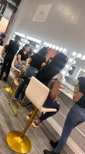 A group of women are sitting in chairs in front of mirrors in a salon.