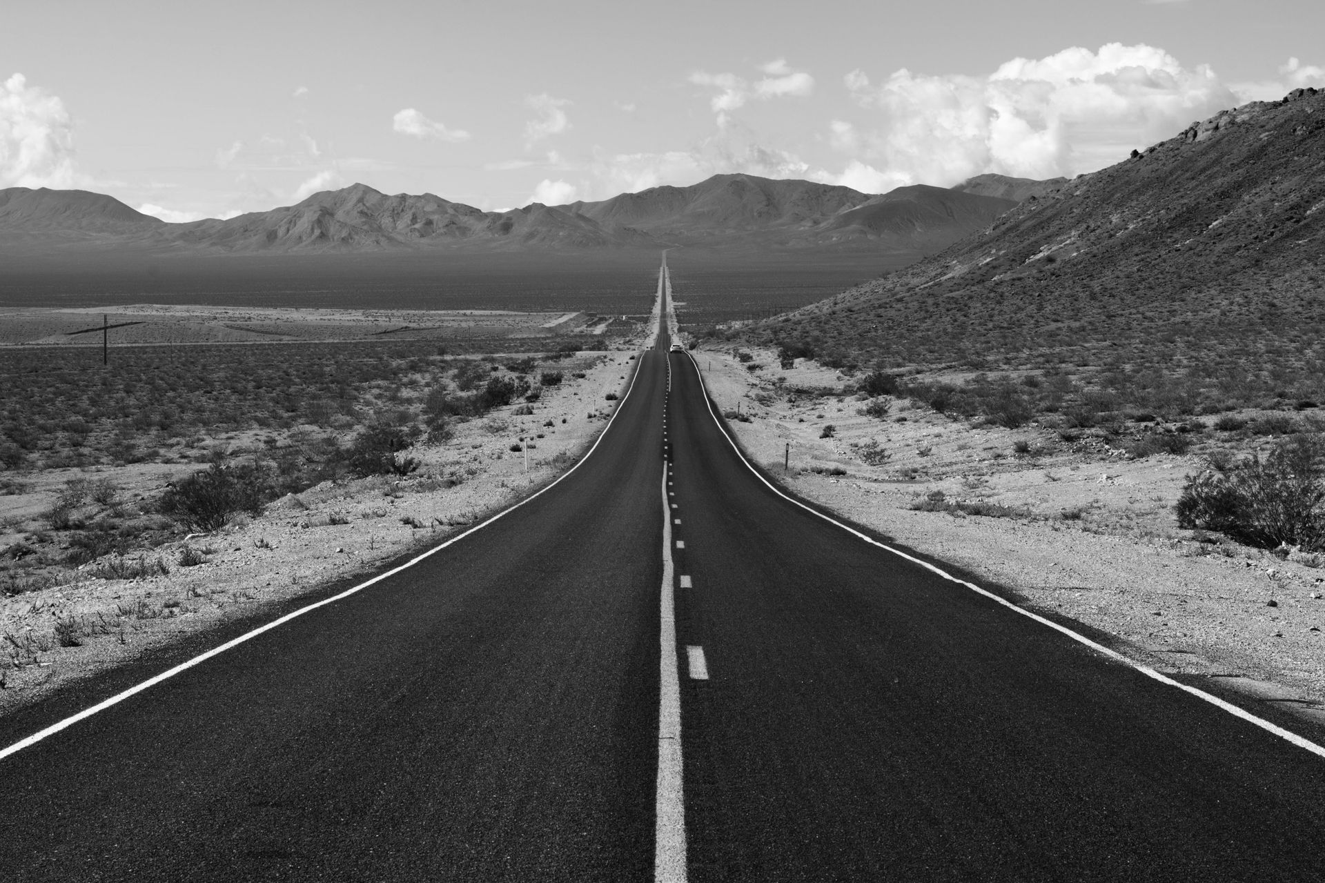 A black and white photo of an empty highway with mountains in the background